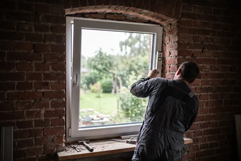 Fenstermontage in einem Backsteinhaus: neues weißes Fenster wird mit der Wasserwaage ausgerichtet